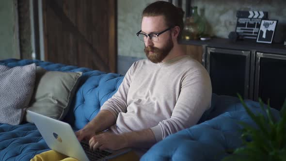 Hipster Male Freelancer Typing on Laptop in Living Room