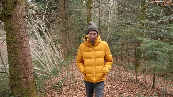 White male with bright yellow coat walks in moody Swiss forest, tracking infront