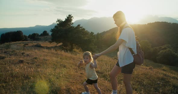 Woman Holding Child Hand and Climbing Mountain on Vacation Travel at Sunset