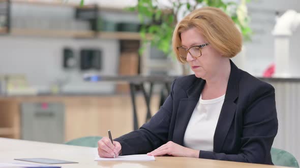 Old Businesswoman Thinking and Writing on Paper in Office