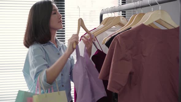 Asian woman shopping clothes. Shopper looking at clothing on the rail indoors in clothing store.