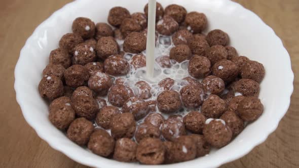 Slow motion pouring milk in bowl of crunchy cereal chocolate balls flakes