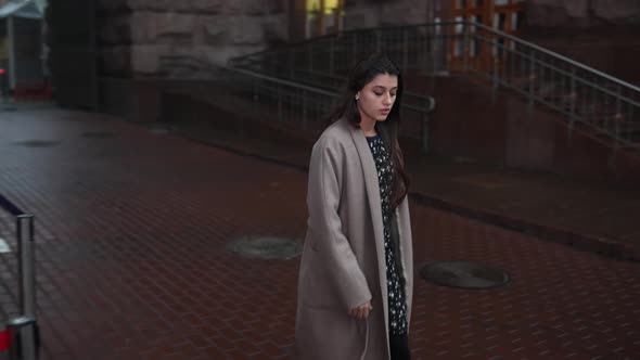 Young Beautiful Girl in a Gray Coat Walking Down the Street