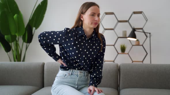 A Young Woman with Back Pain Presses Her Hands to the Small of Her Back Wincing From the Pain While