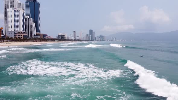 Drone Cinematic Fly Over a Blue Sea with Strong Breaking Waves and Surfers View of Building and