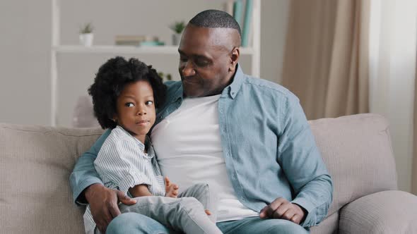 Happy African American Family Adult Father with Little Funny Daughter Sitting on Sofa in Room