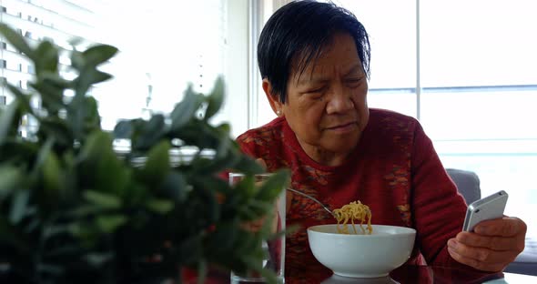 Senior woman using mobile phone while having food