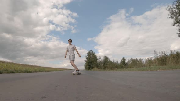 guy longboarding riding skateboard cruising downhill on countryside road on summer sunny day