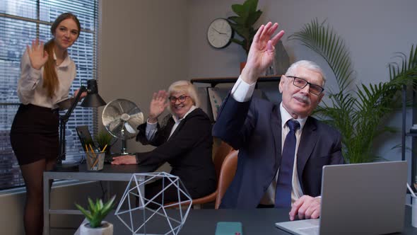 Senior Businessman with Colleagues Team Waves Palm in Hello Gesture Welcomes Someone in Office