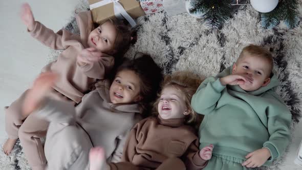 Four Sweet Children Lay Down Jn a Carpet Near Christmas Tree and Waving Their Legs and Hands