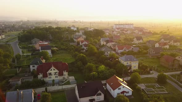 Aerial view of rural residential area with private homes between green fields at sunrise.