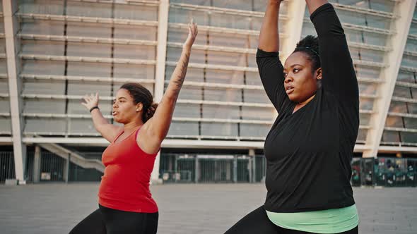 Two Peaceful Overweight African American Female Friends Practicing Yoga Outdoors Doing Breathing