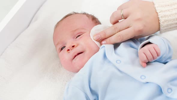 Closeup of Mother Cleaning Face and Eyes of Her Newborn Baby Son with Cooton Pad