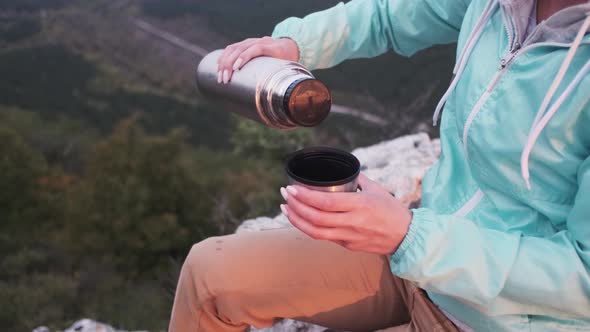 Traveler Woman Pouring Tea From Thermos to Cup in Mountains