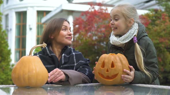 Girl Brings Pumpkin Jack-O-Lantern to Mother in Yard, Preparation for Halloween