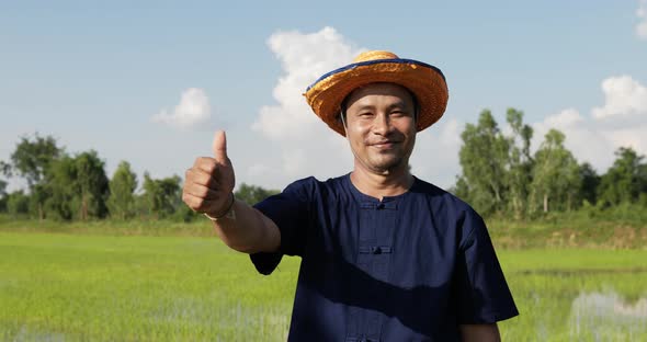 Handsome farmer standing and thump up in rice field