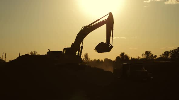 Silhouette of an Excavator That Loads Sand Into a Truck at Sunset. Concept Construction and Heavy