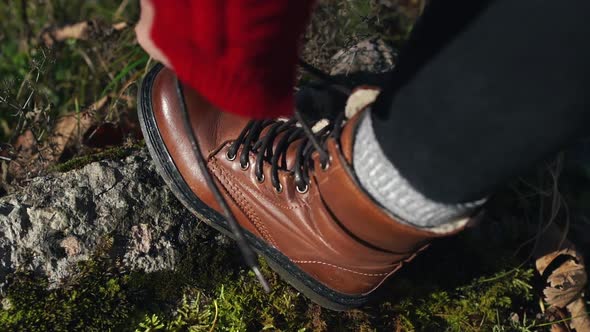 Young Caucasian Traveling Woman with Backpack Tying Up Shoe Laces on Her Boots on a Pathway in