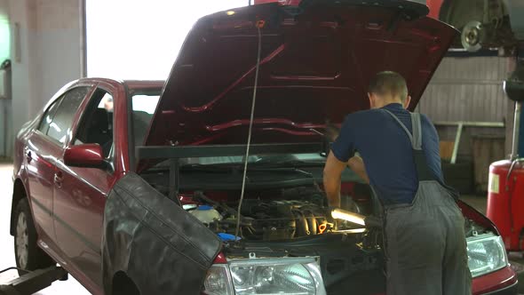 Repairman Auto Service Worker Installing Protective Mechanism Under the Car Hood