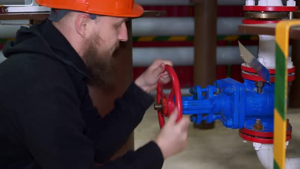 A Bearded Worker in a Helmet Turns the Valve to Supply Fluid to the System