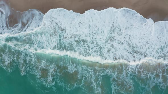 Drone flight over wild beach and turquoise green sea, above waves and sand