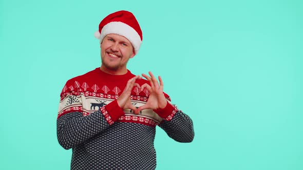 Smiling Man in Christmas Sweater Makes Heart Gesture Demonstrates Love Sign Expresses Good Feelings