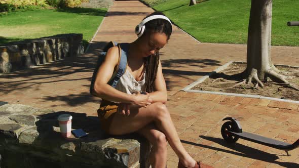 African american woman using smartwatch sitting and wearing headphones in park