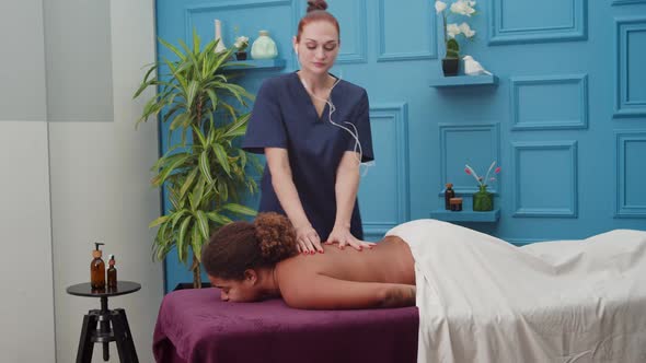 Masseuse Listening to Music Dancing While Massaging Woman Indoors