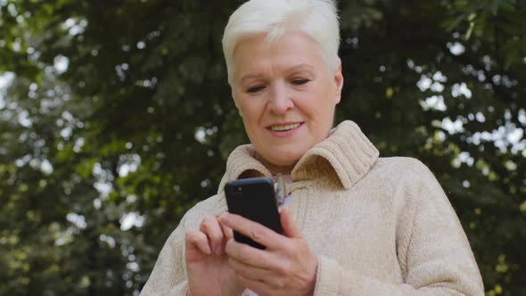 Smiling Mature 60s Woman Texting Messaging on Modern Smartphone Gadget Happy Senior 70s Grandmother