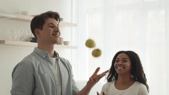 Diverse Couple Having Fun Cooking Juggling Apples In Kitchen Indoors