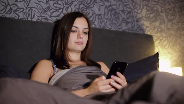 Girl Surfing Internet While Lying in Bed in the Bedroom at Night, Wrote Sms, Looks Photo, Chating