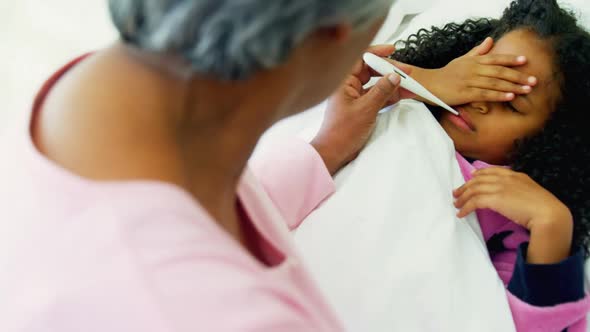 Grandmother checking temperature of sick granddaughter in bed room