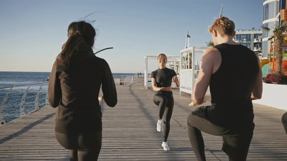 Fitness Coach Showing Cardio Exercise to Group of Sporty People Running on Place on Pier Enjoying