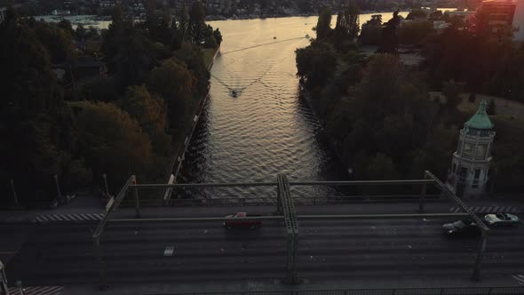 Drone Following Boats Cruising Montlake Cut Under Bridge With People Driving Cars At Sunset