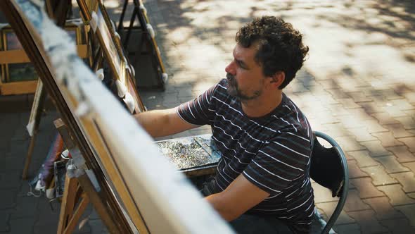 Mature Guy Artist Drawing Picture with Marine Landscape and Sailing Ships While Sitting in Park