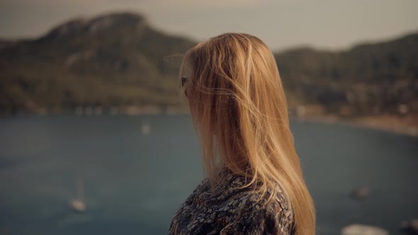 Hair Flying On Sea Breeze Wind. Girl Sitting On Cliff And Looks At The Sea. Woman Sitting On Rock.