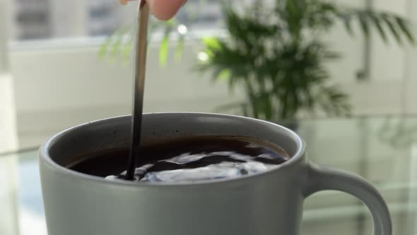 Stirring hot cup of coffee with a spoon, close up. Drop of coffee fall in a mug