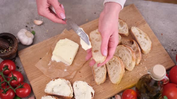 Woman Smearing Soft Butter on Slice of Baguette Bread By Knife at Domestic Kitchen