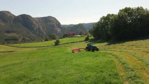 Tractor Making Windrows Of Grass For Silage In Countryside Field Of Hjelmeland In Norway. - aerial p
