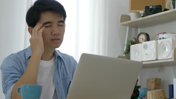 Young Asian businessman working on laptop at office, feeling tired and having headache.