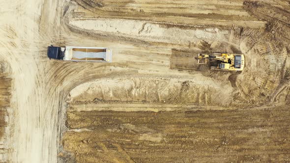 Aerial top down view of an excavator loading crushed stone into a dump truck in a crushed stone quar