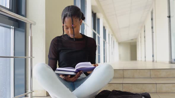 Young African Woman Student Sitting on the Floor with a Books in a Modern Library