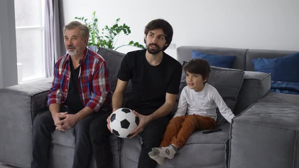 Three Generations of Men Relax on Couch in Living Room Watch Football Match