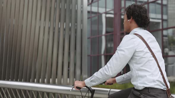 Businessman in Earphones Riding Bike on City Street