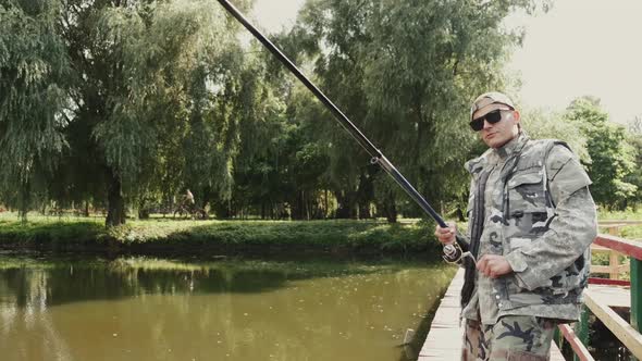 Man in Special Uniform Fishing on a Wooden Pier in a Park