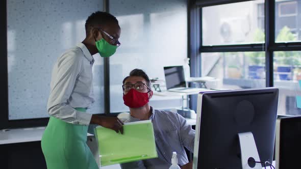 Diverse male and female office colleagues wearing face masks discussing at modern office