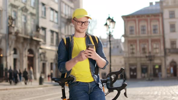 Portrait of a Happy Delivery Man Who is Sitting on a Bicycle and Texting on a Smartphone