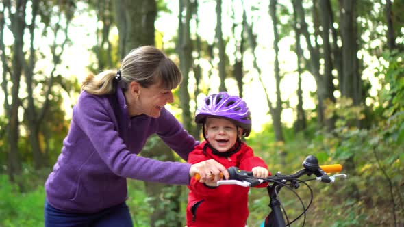 Closeup. Mama teaches her little son to ride a bike. Happy boy. Moving camera.