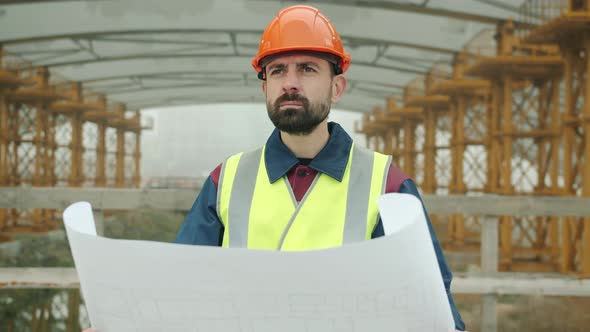 Portrait of Foreman Wearing Uniform Checking Blueprint and Looking at Construction Site Outdoors