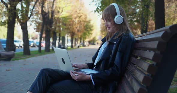 Young Cute Girl Sits on the Street and Types on a Laptop Keyboard